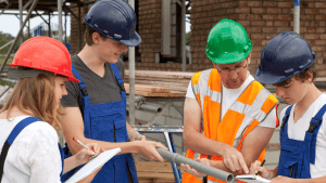Photo of four people with hard hats on looking at building plans.